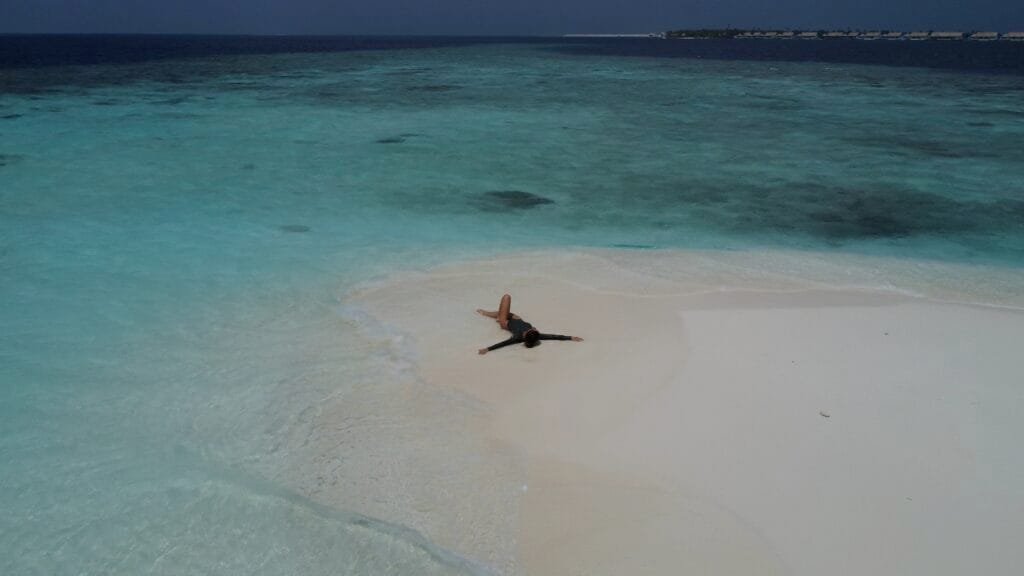 A person relaxing on the sandy shores of a beautiful Maldives sandbank, enjoying the tropical paradise.