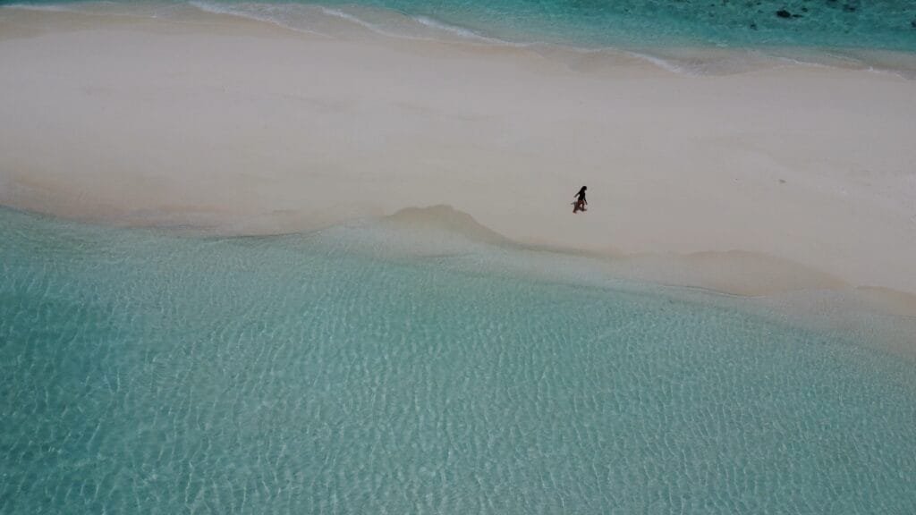Aerial view of a person strolling along a pristine sandbank beach in the Maldives, surrounded by turquoise waters.