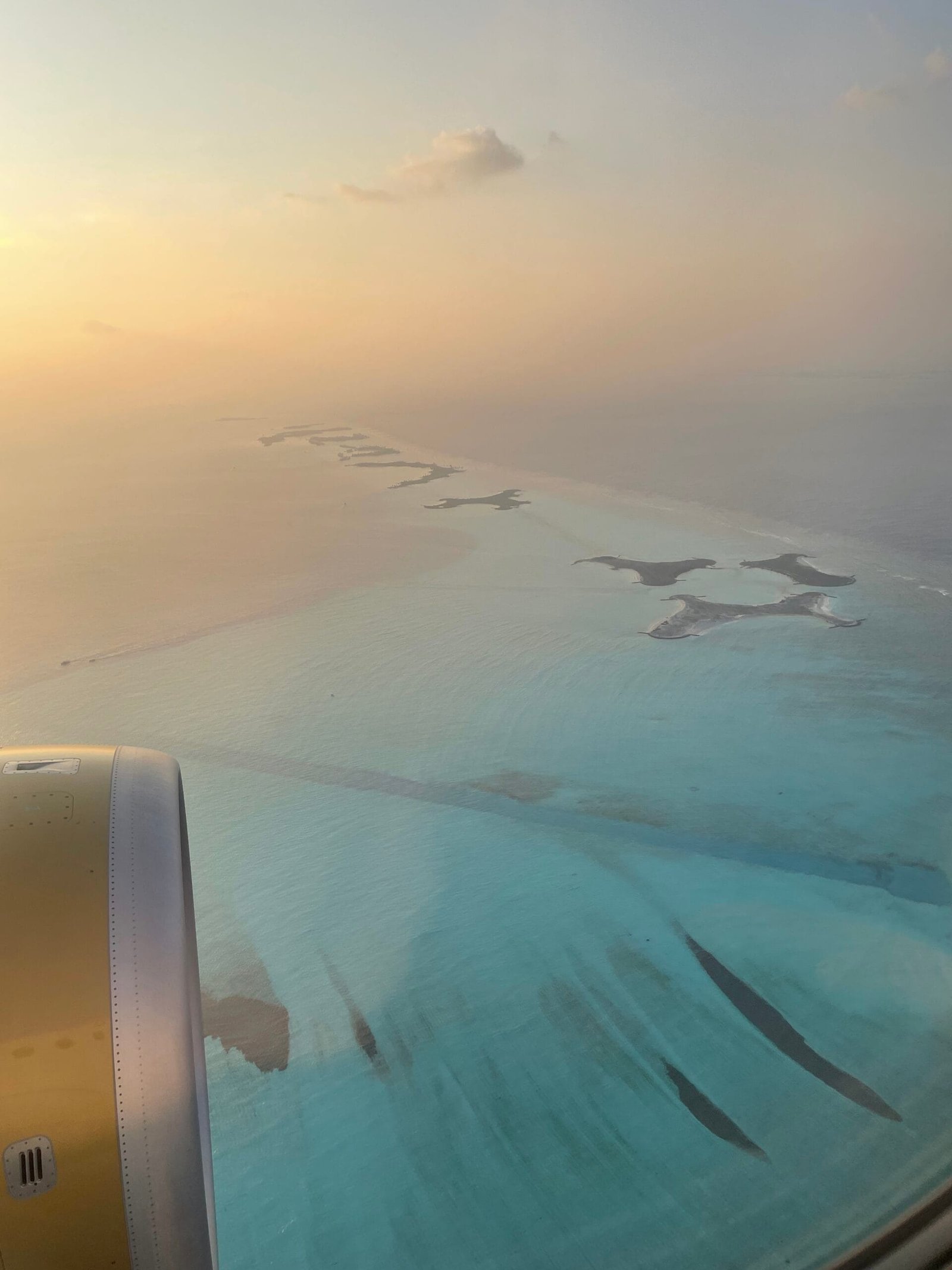 An airplane wing viewed from a window, with the stunning Maldives landscape visible below.