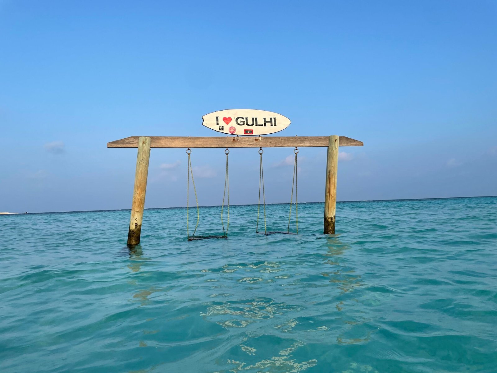 A swing hanging over water with a sign above it, set in the beautiful Maldives, Gulhi.