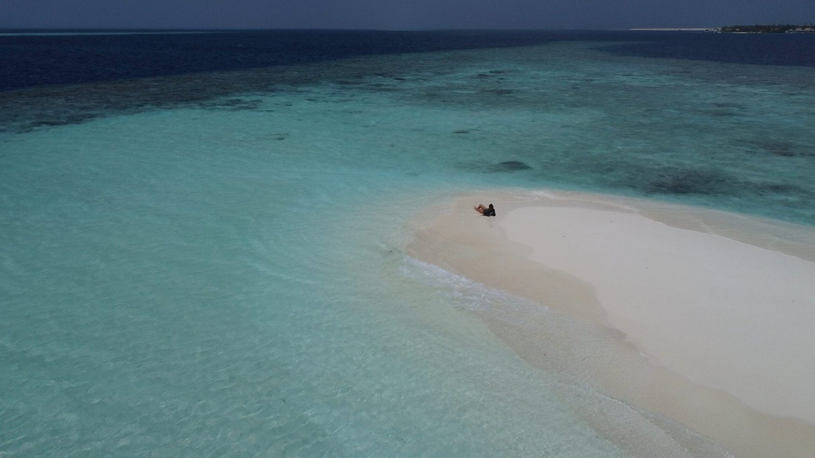 Eine Person sitzt auf einer Sandbank in den Malediven.